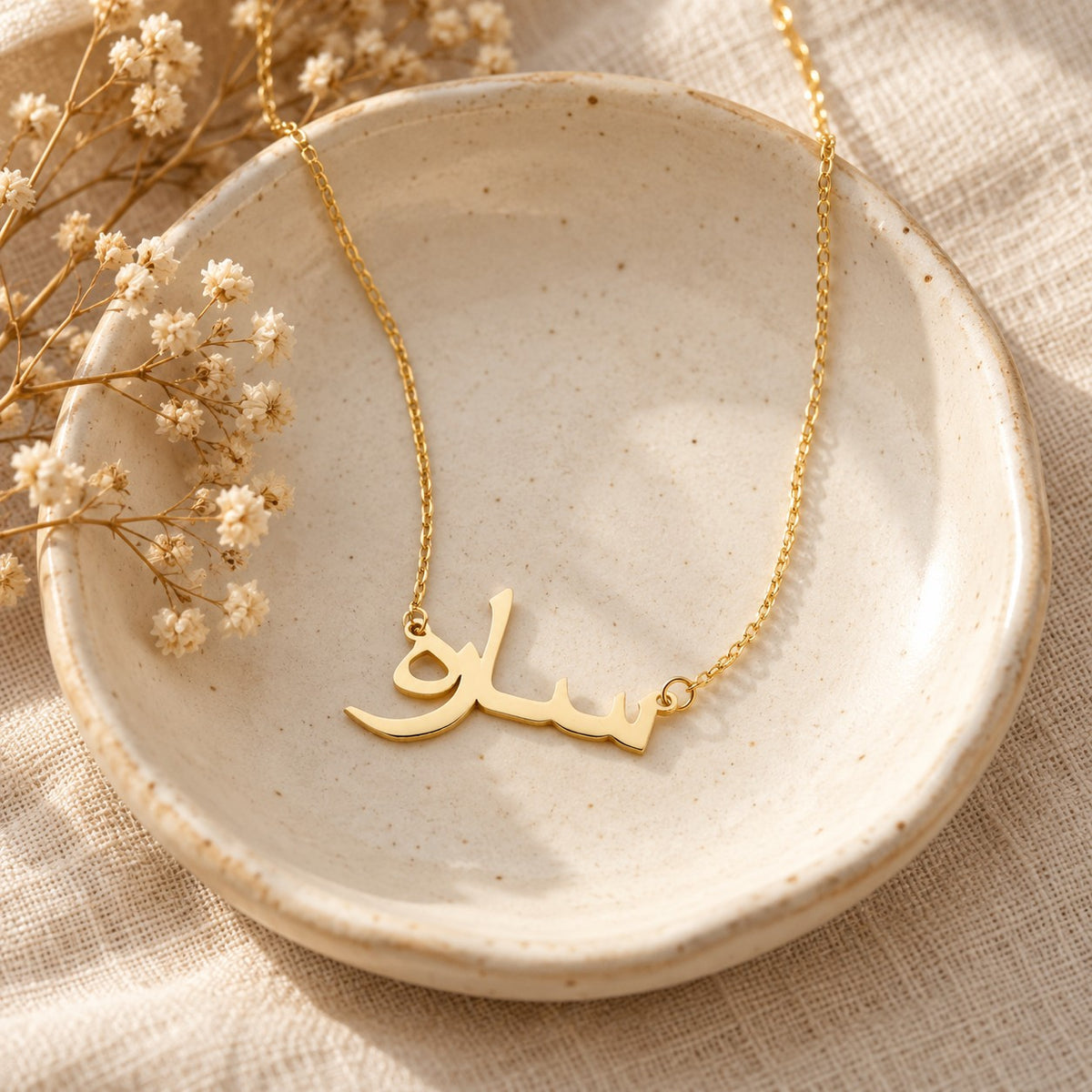 The Custom Name Necklace 18k in a ceramic trinket dish