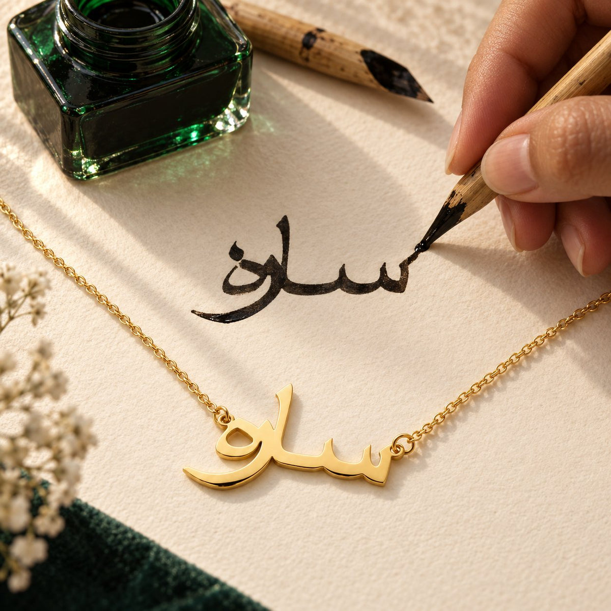 A calligrapher writing an Arabic name in ink above the matching gold name necklace